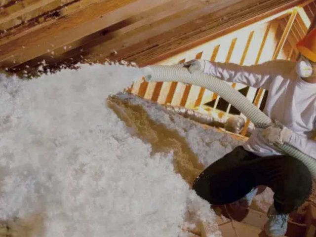 Technician installing blown-in insulation across an attic floor.