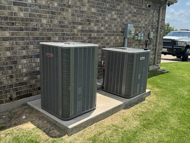 Two residential outdoor air-conditioning condensers installed beside a home.