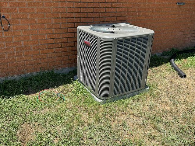 Residential outdoor AC condenser installed beside a brick exterior wall.