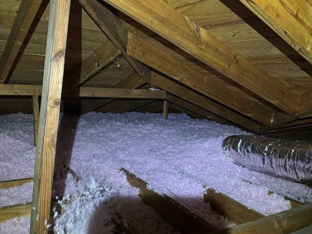 Blown-in attic insulation installed around roof framing and supports.